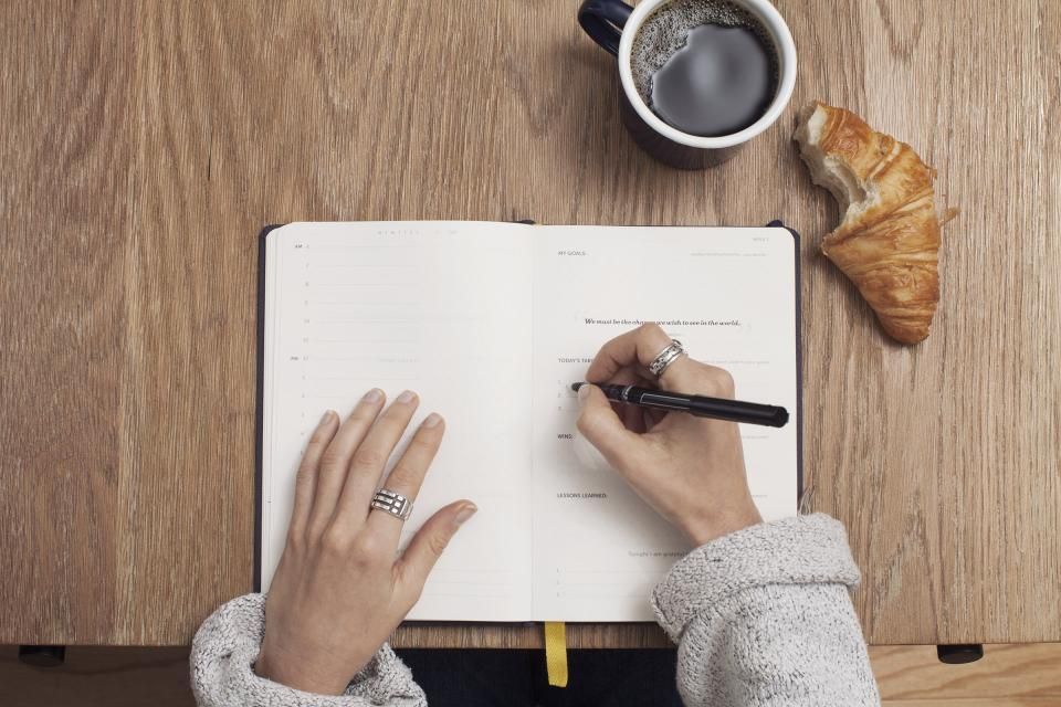 Hands writing in a notebook next to a cup of coffee