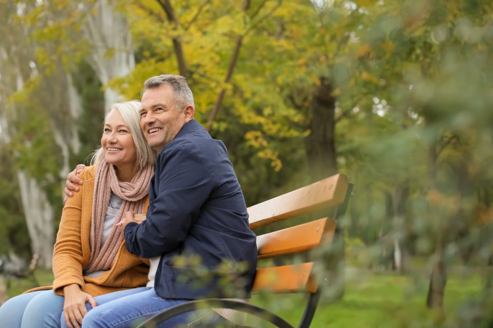 A retired couple sitting together on a park bench in autumn